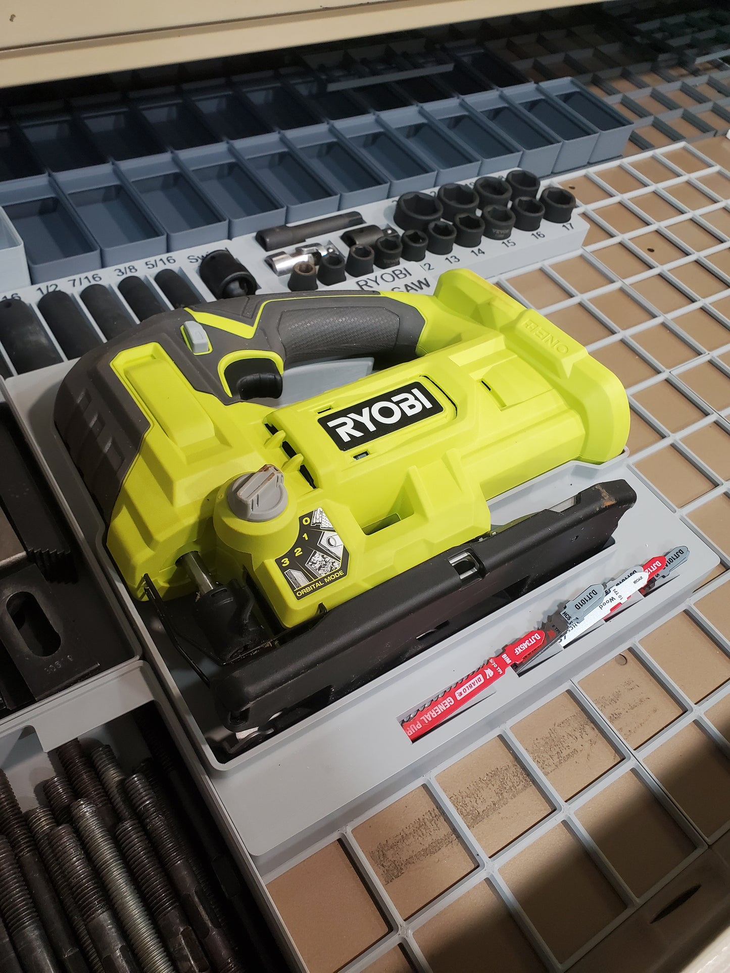 Gridfinity Ryobi reciprocating saw jigsaw module – yellow and black Ryobi jigsaw secured in gray gridfinity tool tray with compartments for blades and accessories