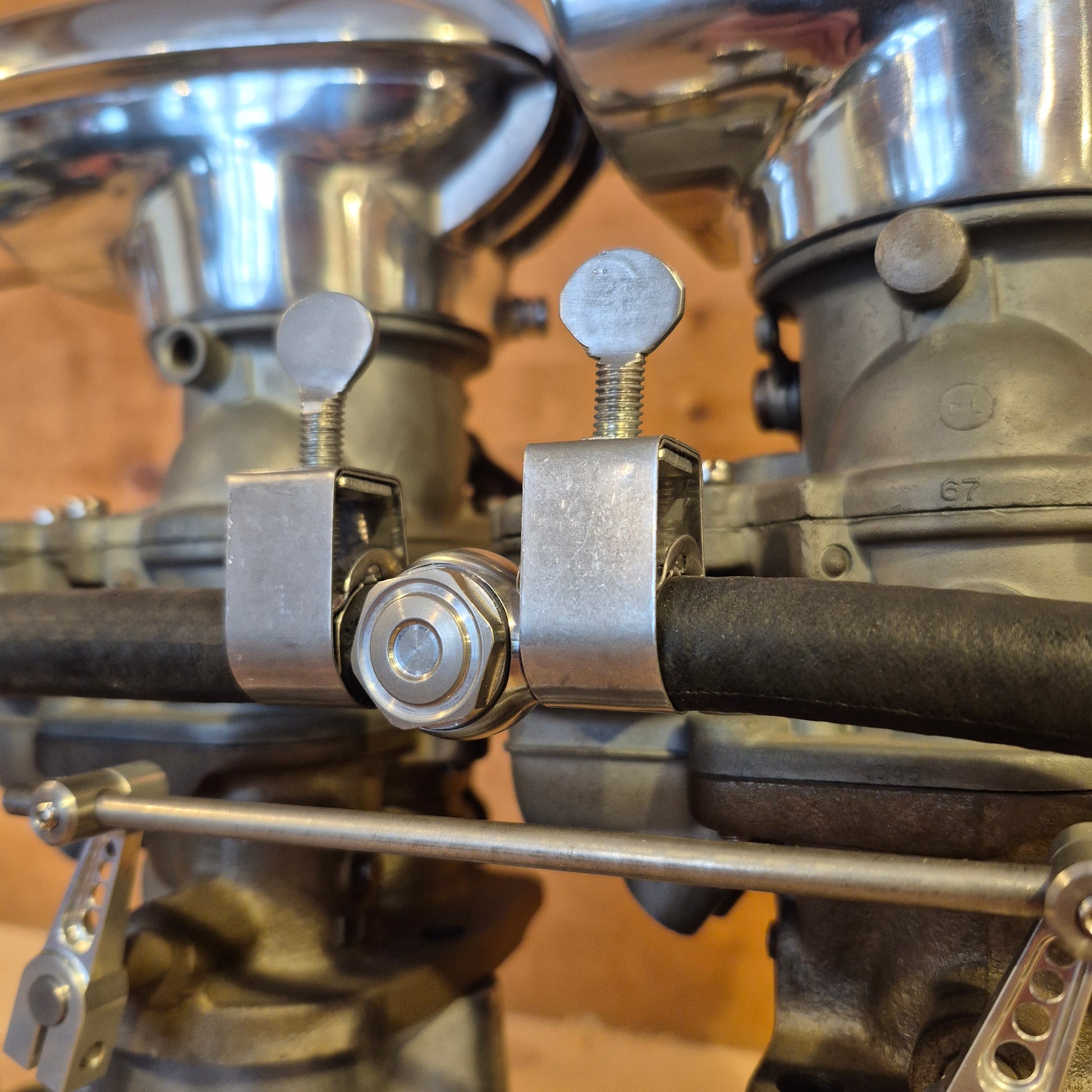 Two Wittek-style stainless fuel hose clamps installed on a Stromberg 97 carburetor fuel log, securing the 5/16-inch fuel hose between dual carburetors on a vintage flathead engine.