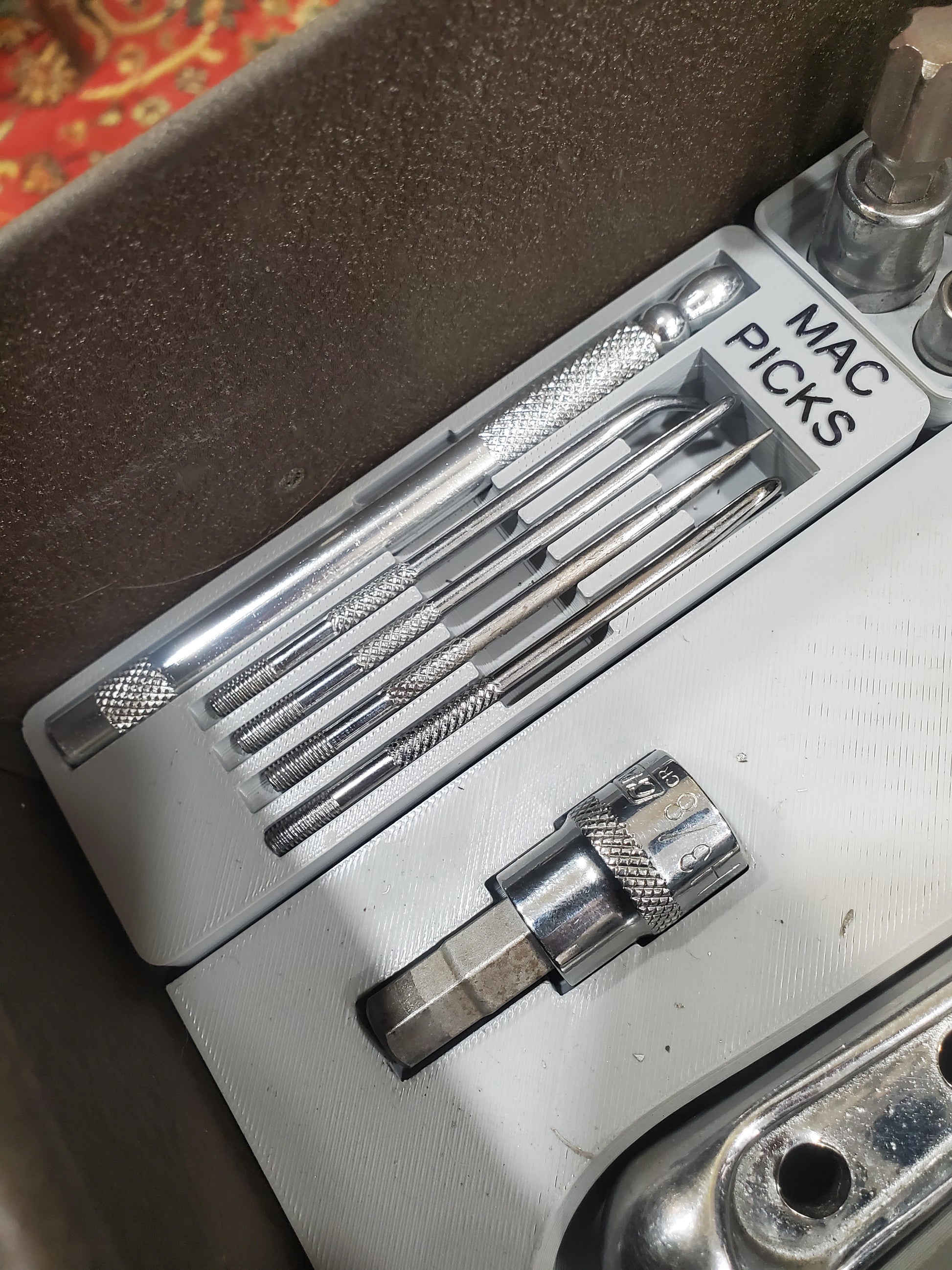 Close-up view of Gridfinity Mac picks holder module filled with metal Mac picks and attachments, demonstrating storage and organization in 3D-printed holder