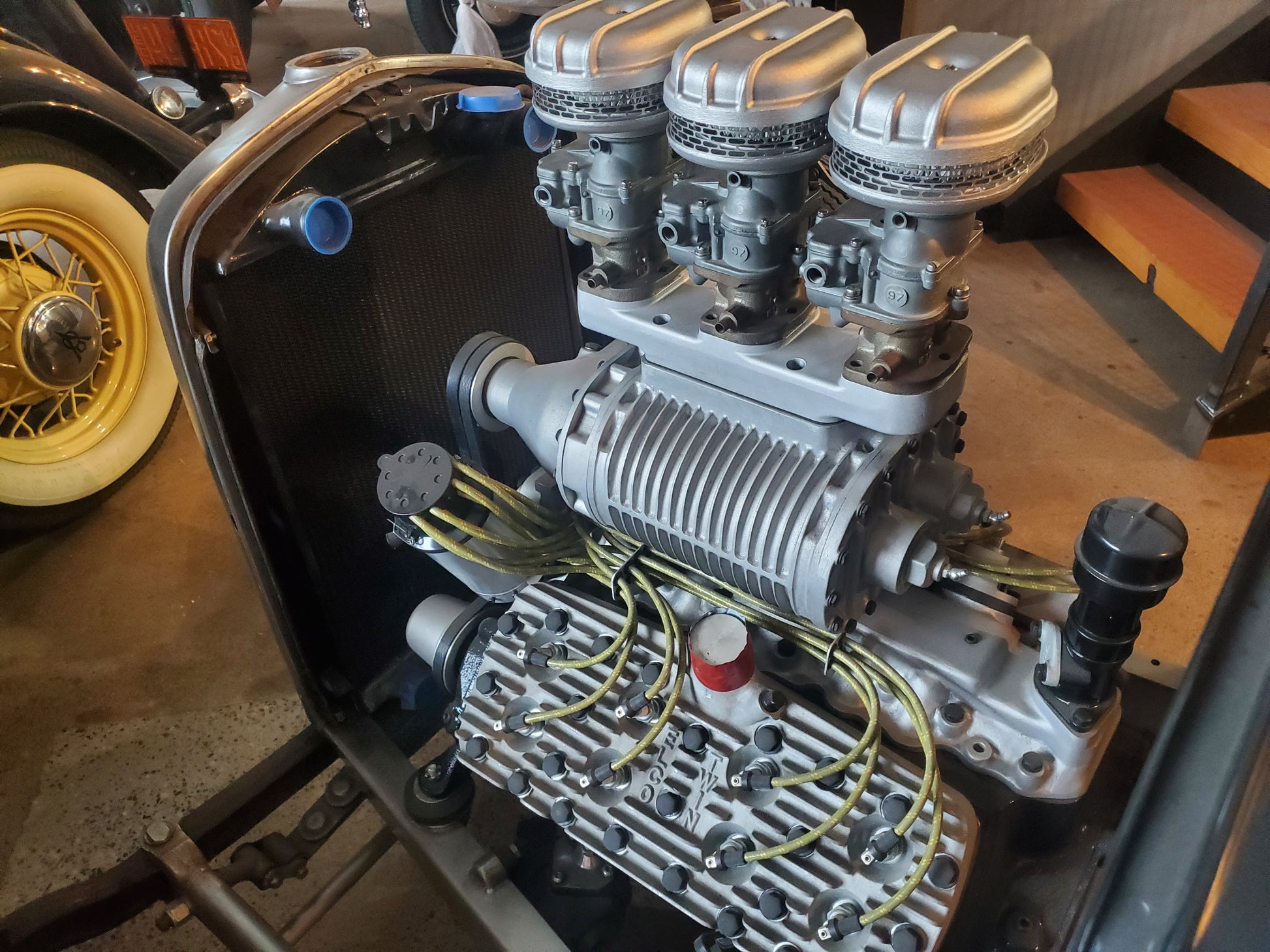 Vintage hot rod engine fitted with S.c.o.T. Italmechanicca 3×2 adapter and supercharger, supporting three Stromberg carburetors with polished scoops, installed in a classic car engine bay with yellow spark plug wires