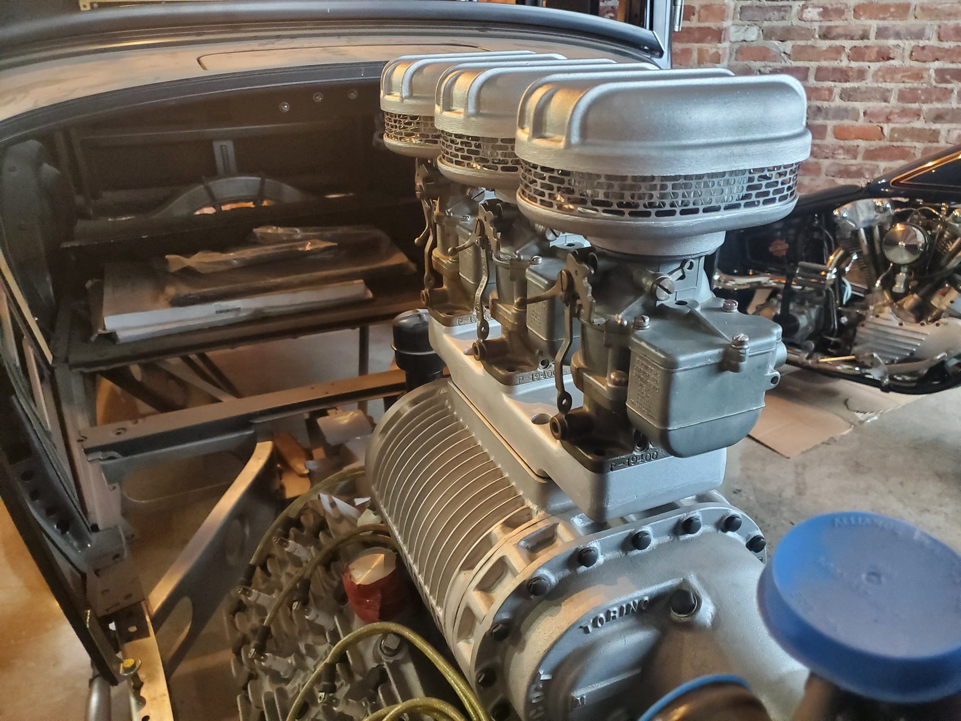 Side-angle view of S.c.o.T. Italmechanicca 3×2 adapter and supercharger installed on a vintage V8 engine, featuring three Stromberg carburetors topped with mesh air cleaners, inside a classic car project